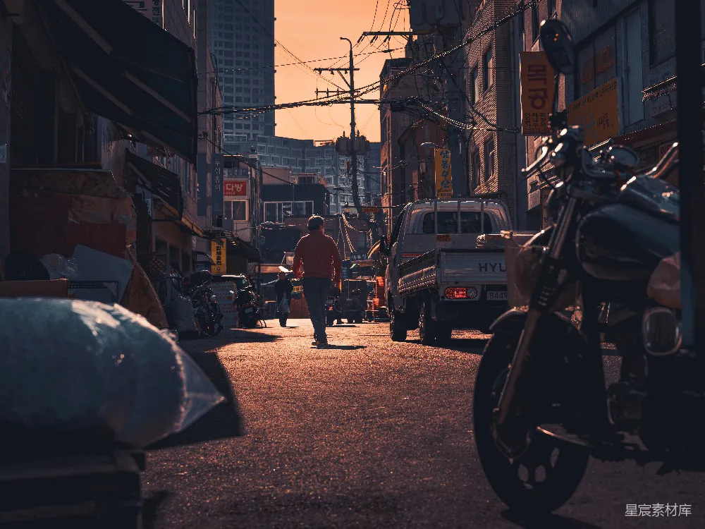 一个男人走在一条街道上，旁边是一辆摩托车。