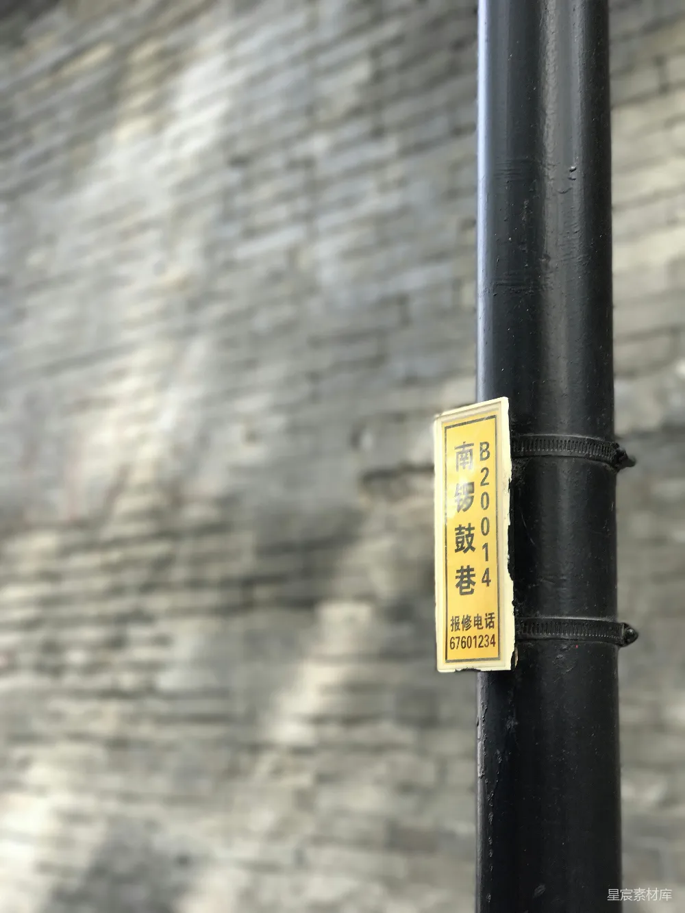 高清摄影  一盏黄色的标志灯挂在黑色的杆子上，背景是一面砖墙。