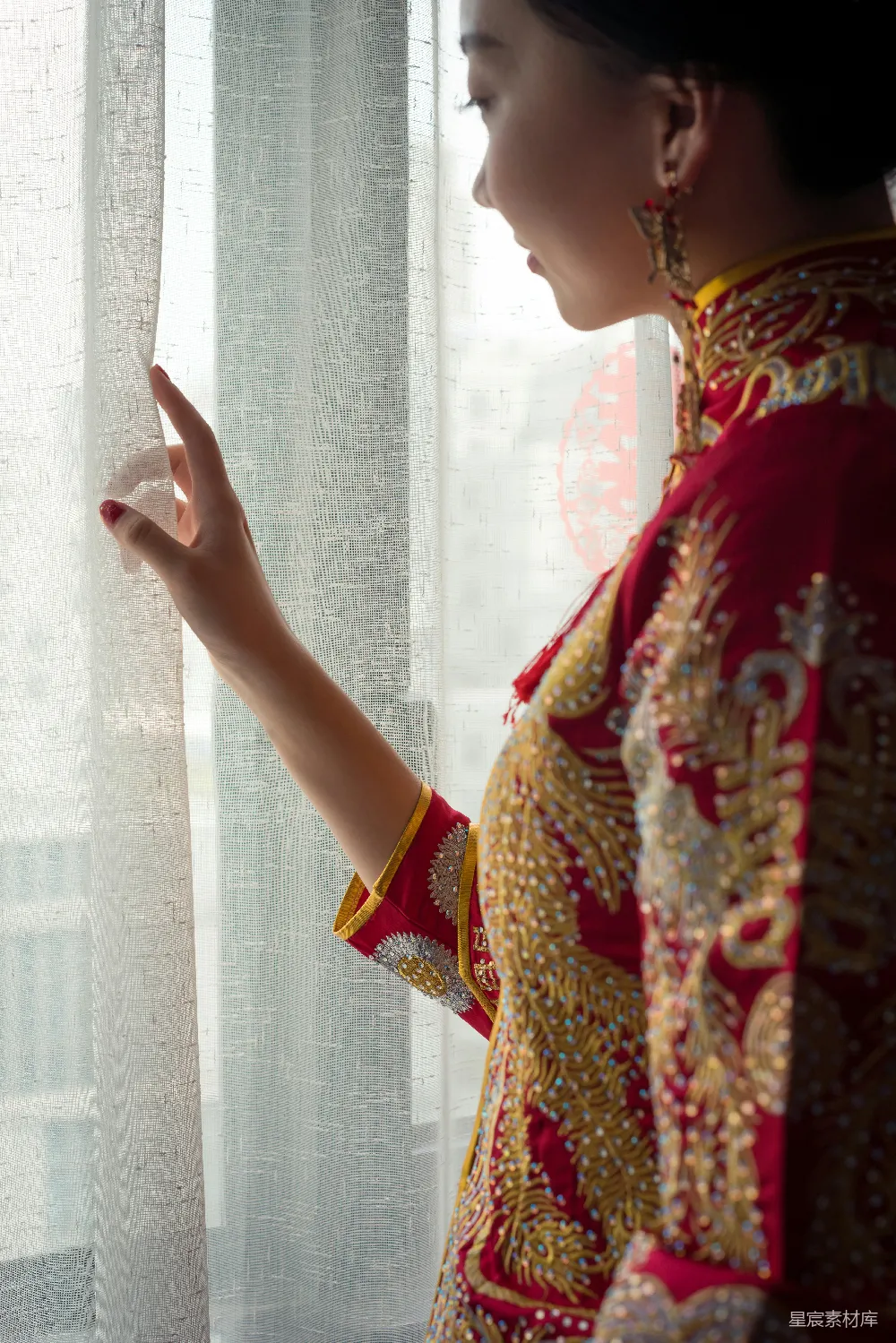 身穿红金色衣服的女人望着窗外。
