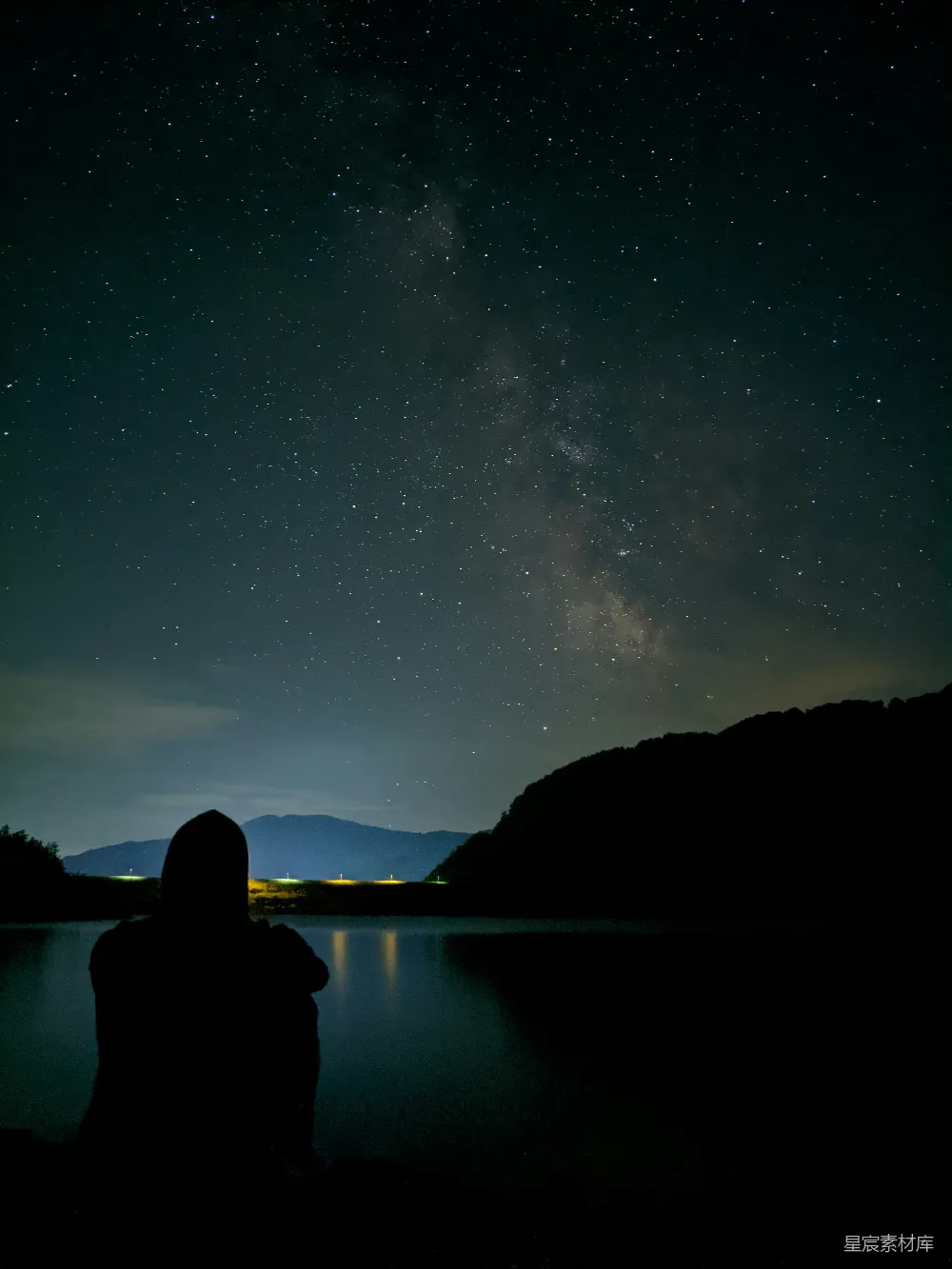 夜晚一个人坐在岩石旁水体附近的轮廓