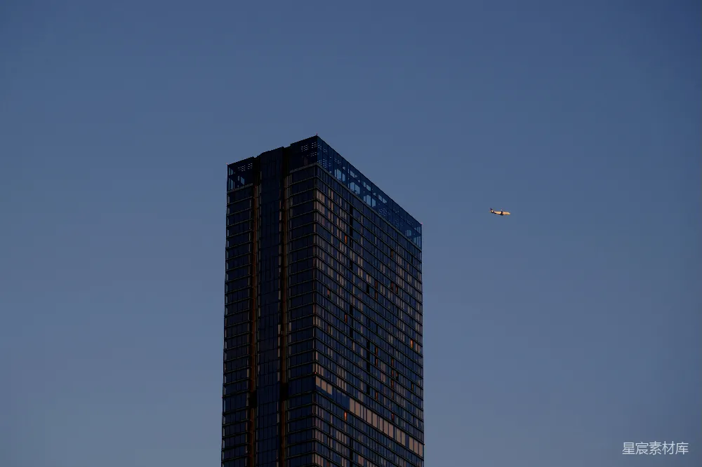 高清摄影  一座非常高大的建筑物，天空中有一架飞机飞过。