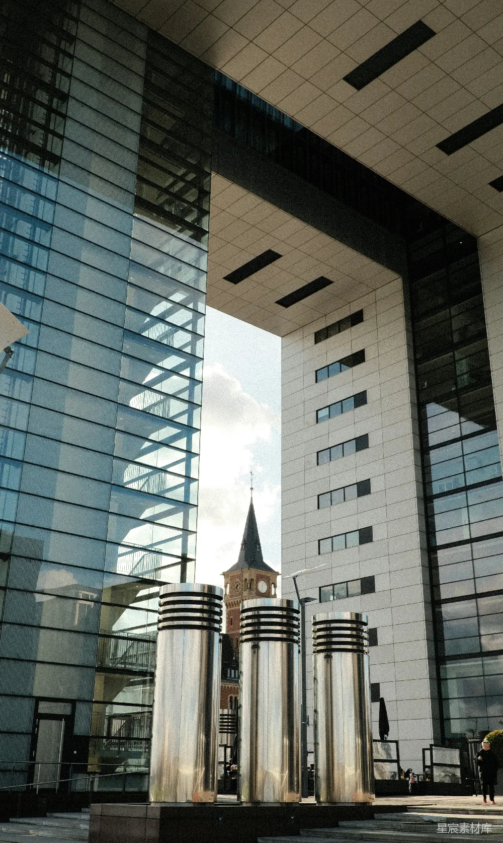 现代建筑环绕着一座教堂塔和圆柱形雕塑。