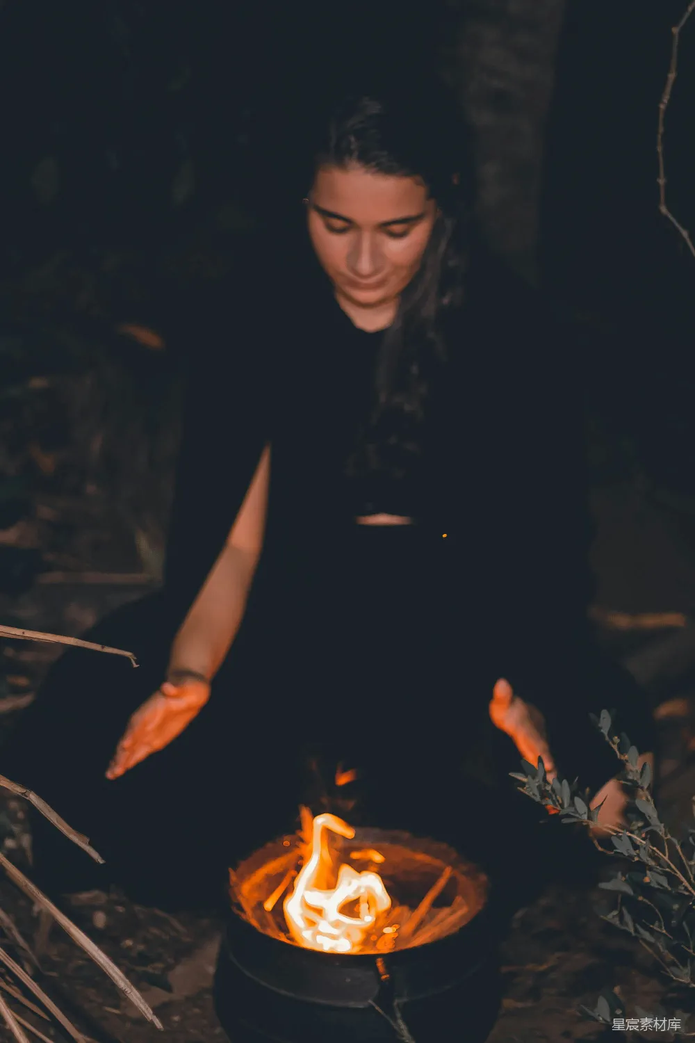 一个女人坐在地上面前有一堆火。