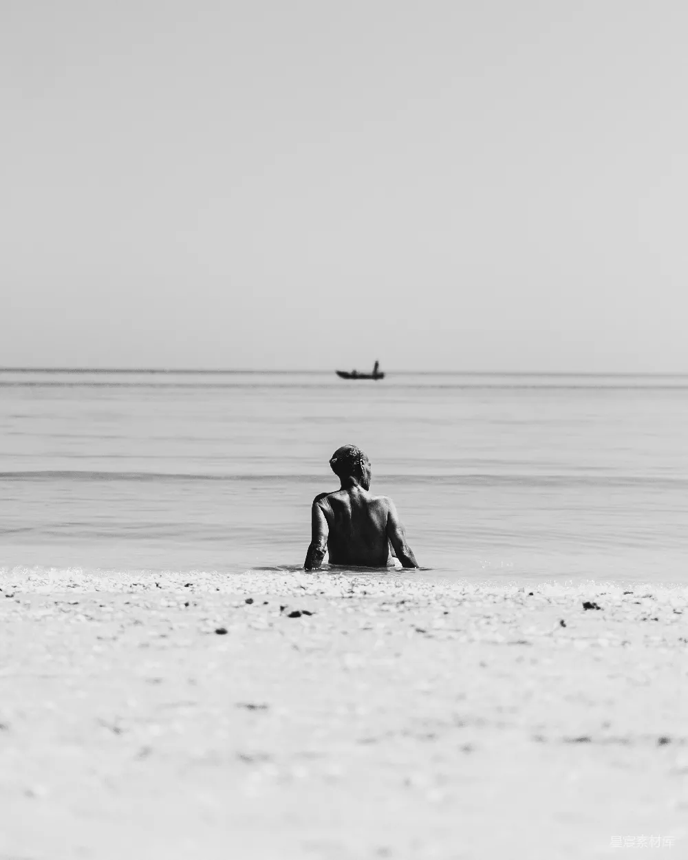 高清摄影  一个人坐在海滩上，背景中有一艘船。
