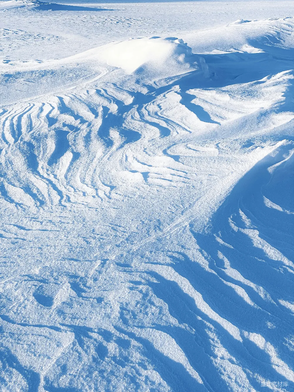 阳光下，雪堆被风吹塑成各种图案。