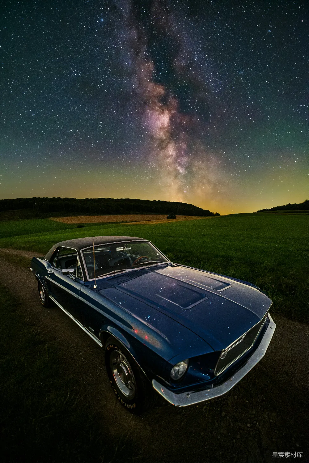 一辆车停在一条尘土路上，在满天星星的夜空下。