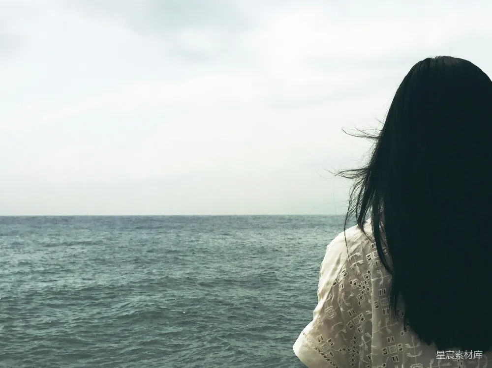 女人面对着一片水域，天空阴沉。