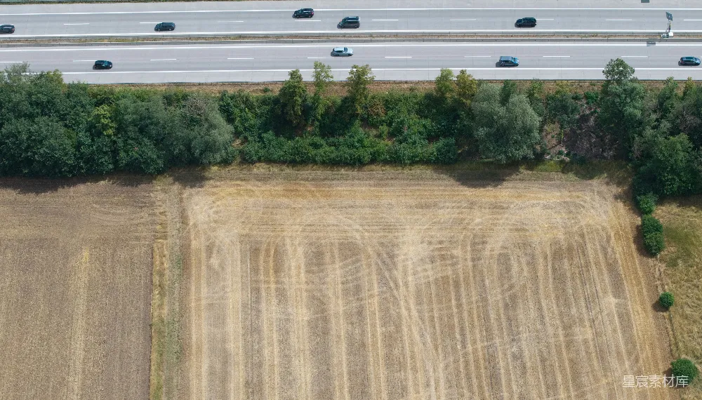 高清摄影  公路沿着树木和收获过的田地延伸。