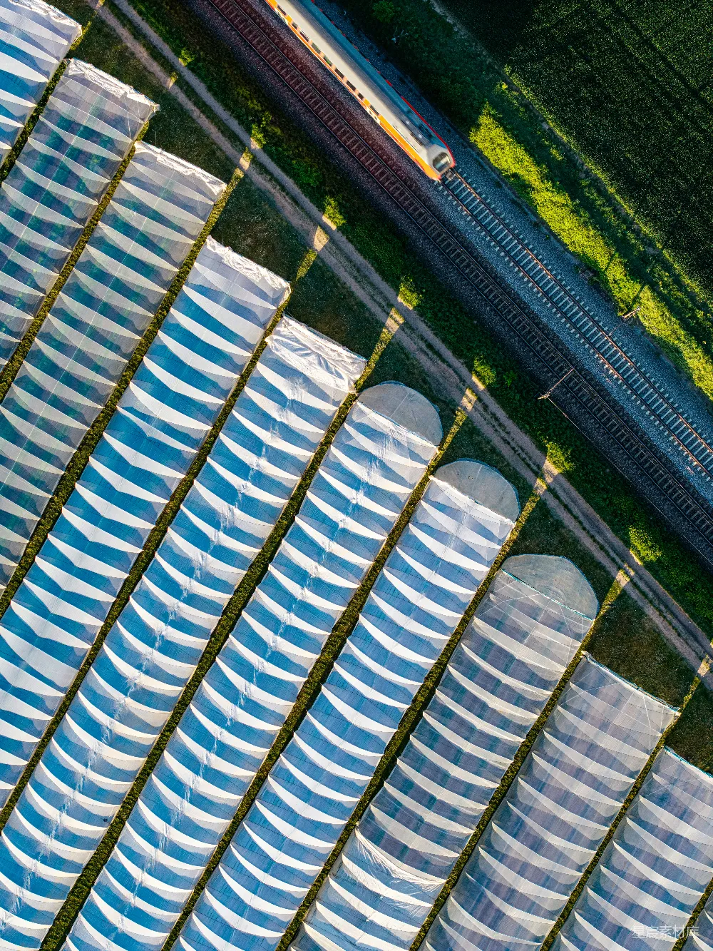 高清摄影  火车从上方经过温室和绿色田野。