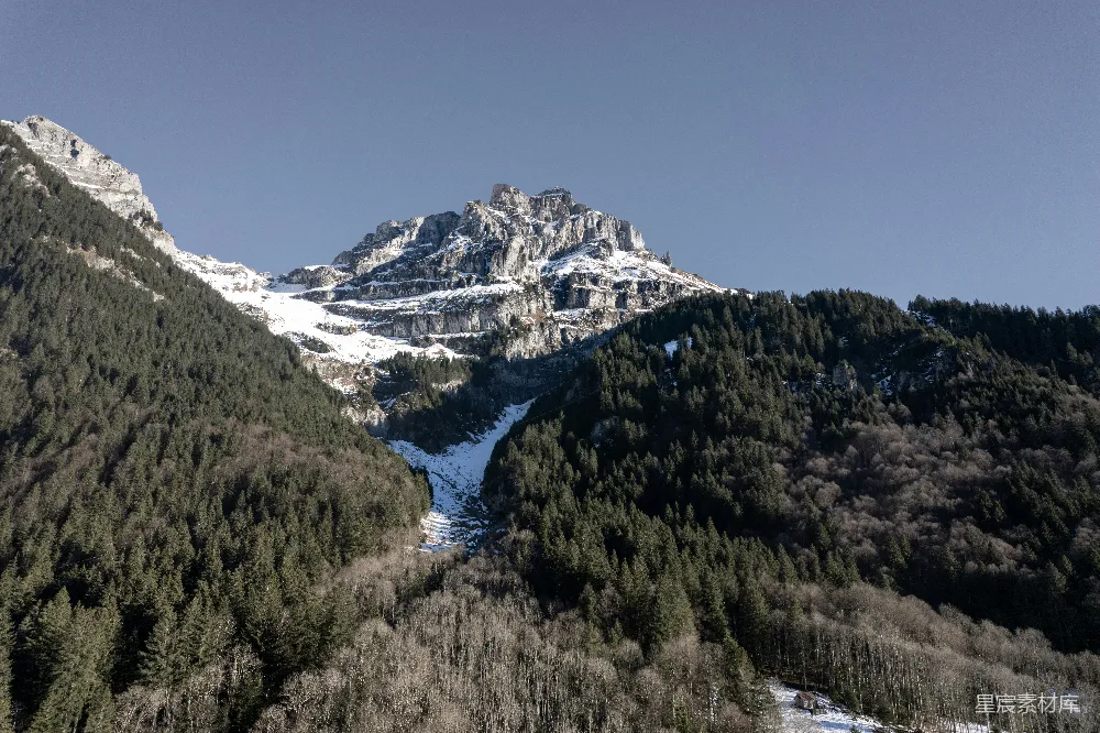 高清摄影  一座被雪覆盖的山峰，山脚下有一片森林。