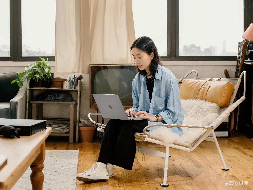 高清摄影  穿蓝色衬衫的女人坐在白色椅子上使用Surface笔记本电脑。