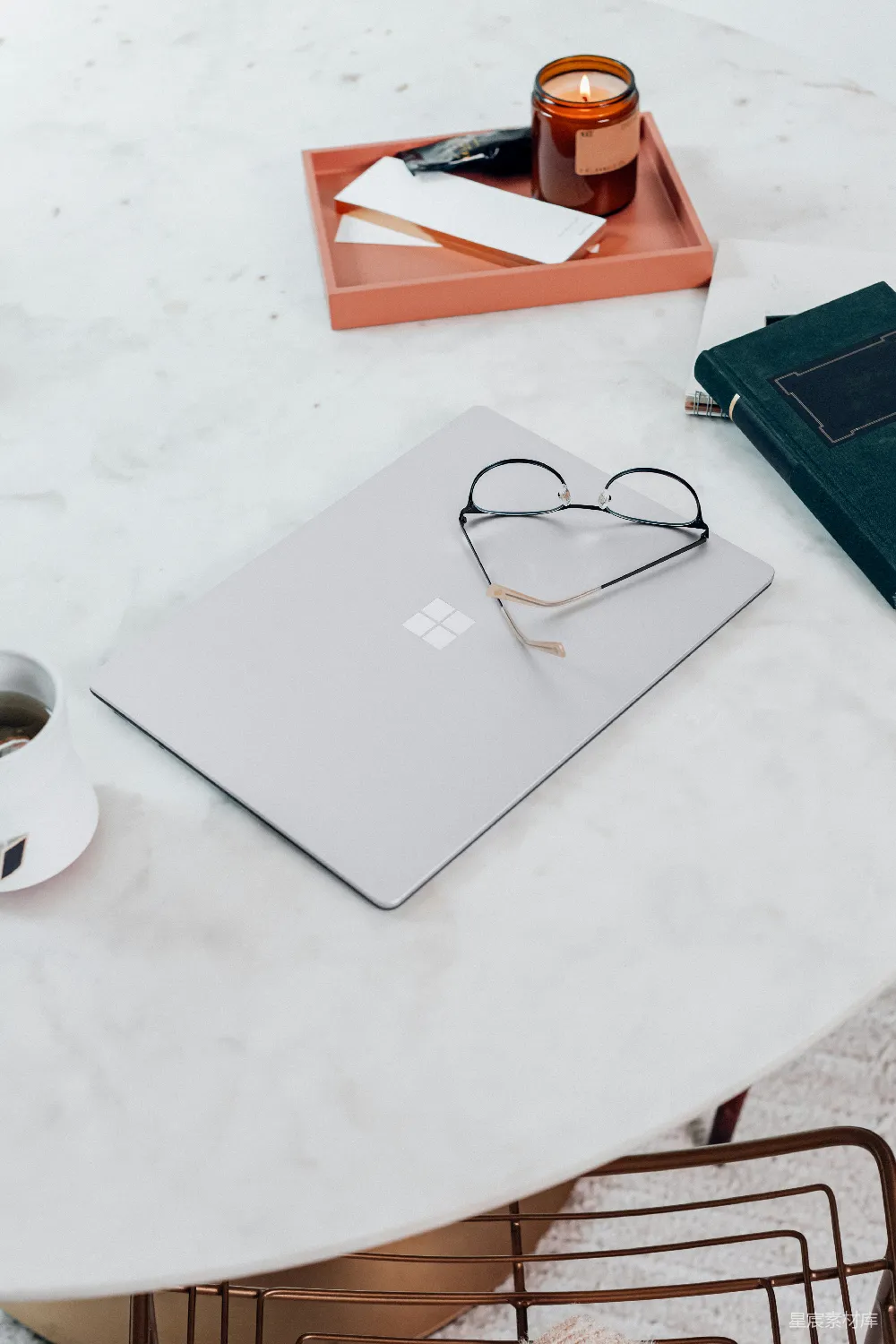 高清摄影  银色的Microsoft Surface Laptop 3在白色桌面上，旁边放着一副黑色框架的眼镜。