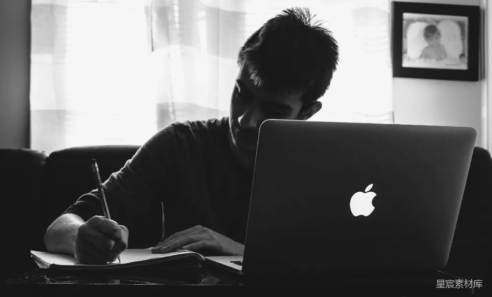 高清摄影  黑白色调的摄影作品，展示了一位男人在MacBook前写字的场景。