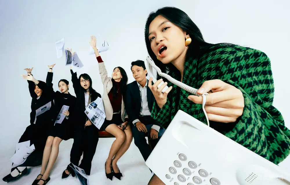 高清摄影  气愤的女性手持电话听筒，同事在背景中。