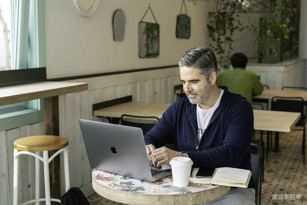 高清摄影  穿着蓝色毛衣的男人坐在桌子旁使用MacBook。