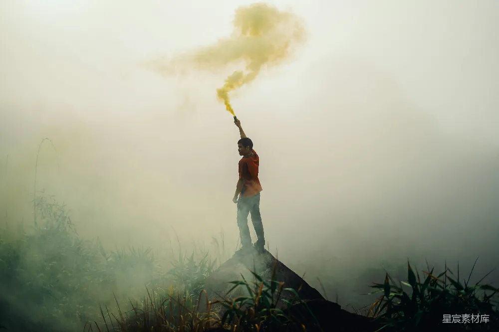 高清摄影 人物 一个站在岩石形成的男人拿着黄色的信号弹，周围是雾气。