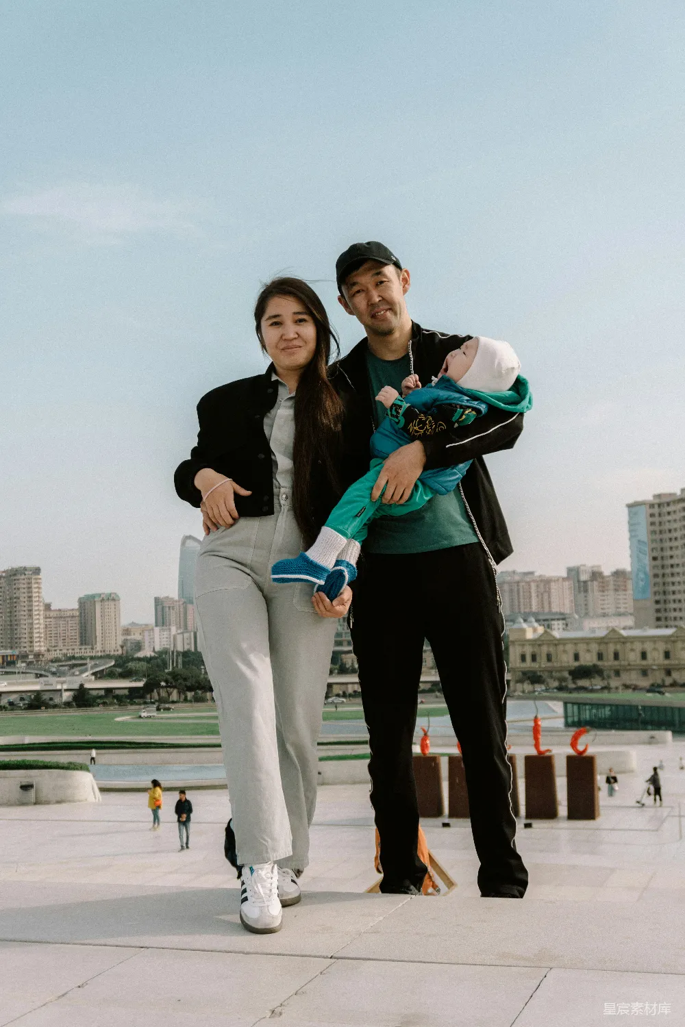 高清摄影  带着婴儿的家庭在户外摆姿势，背景是城市景观。