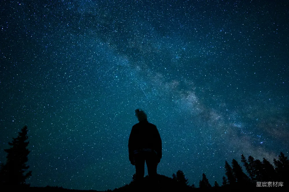 高清摄影  一个男人站在山顶上，脚下是满天星辰的夜空。
