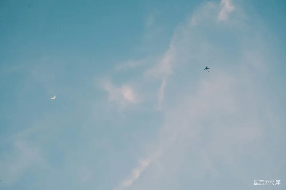 高清摄影  一架飞机在空中飞行，背景中有半轮明月。