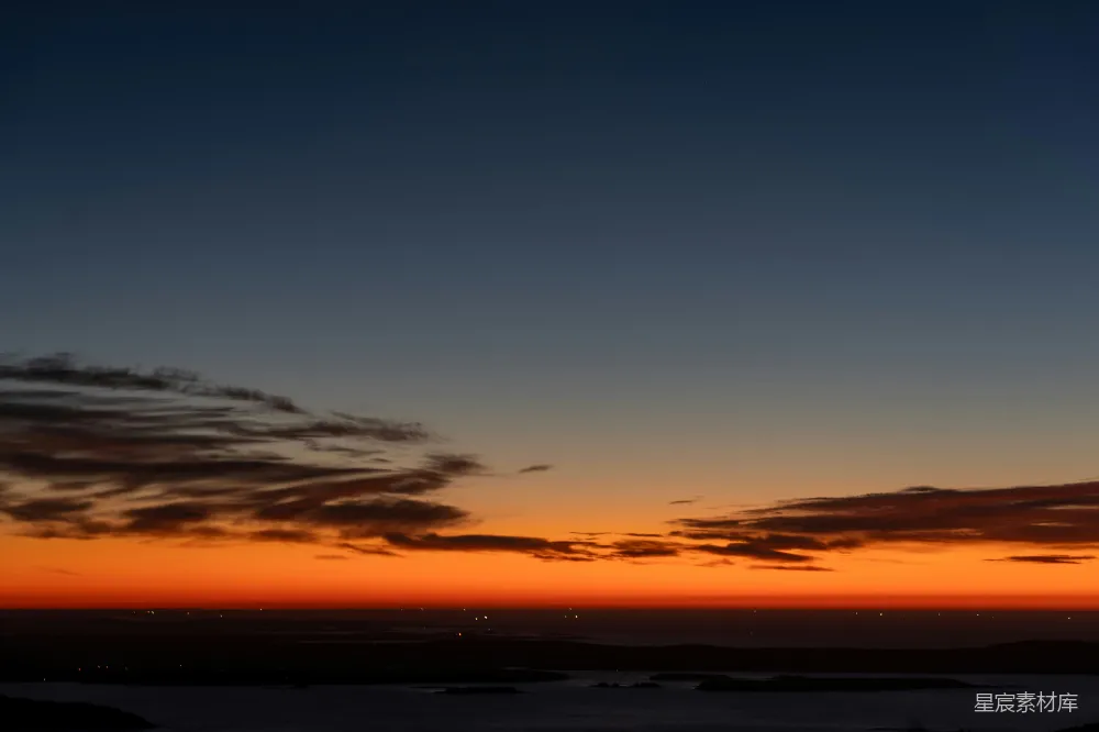 高清摄影  夕阳照耀在平静的海洋上，远处的灯光闪烁。