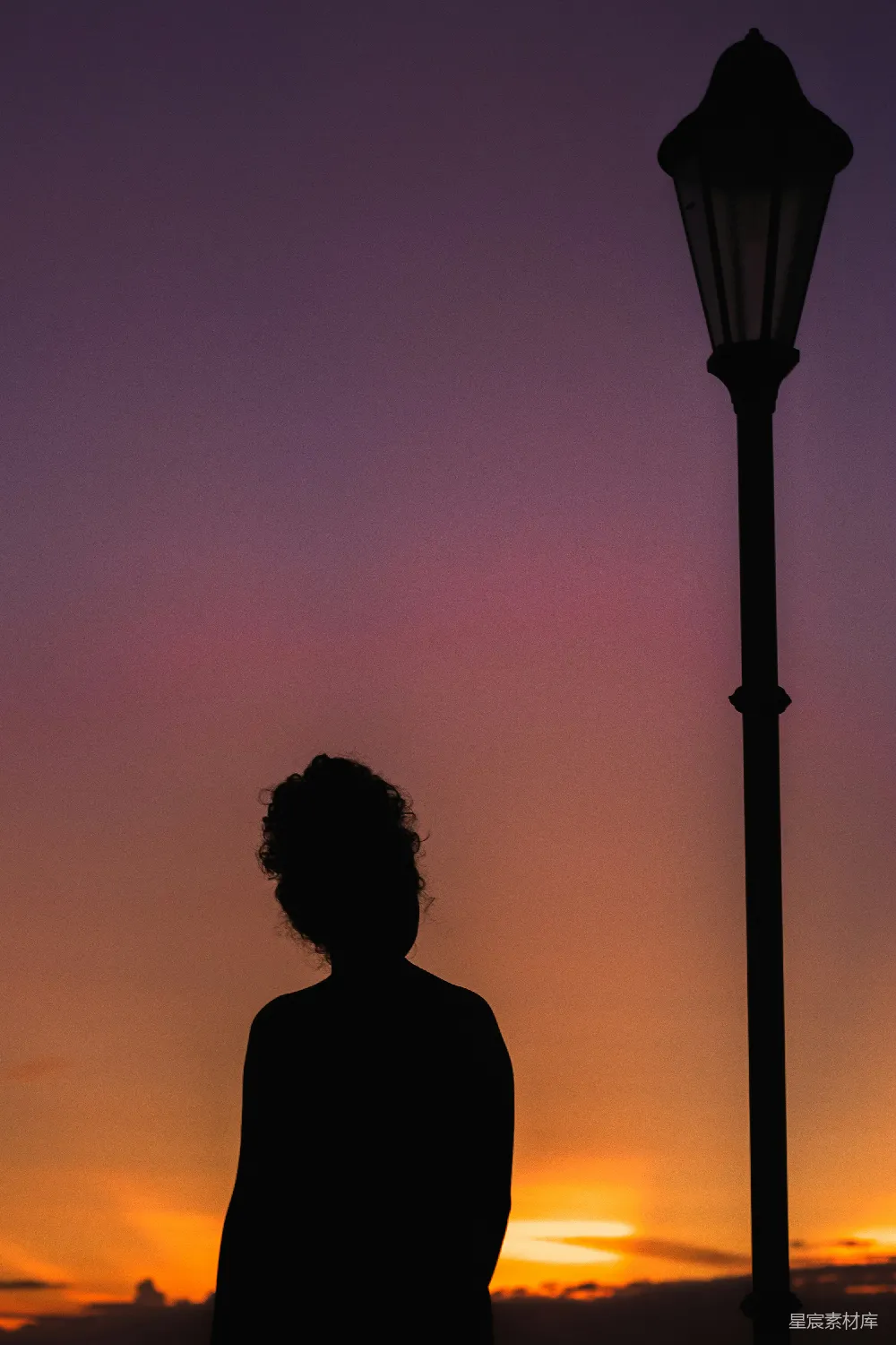 高清摄影  一个女人站在路灯旁边，夕阳西下。