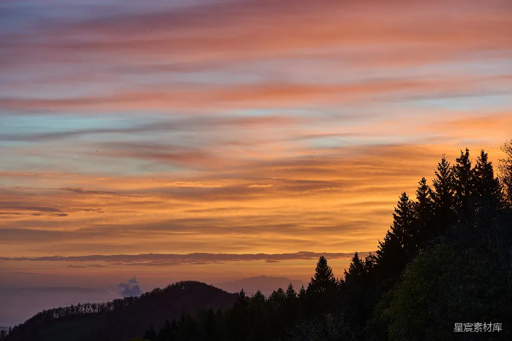 高清摄影  彩霞满天的夕阳映照着剪影的树木和山丘。