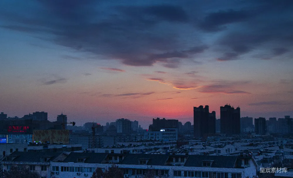 高清摄影  夕阳西下，橙色与灰色的云层下，城市天际线的轮廓清晰可见。