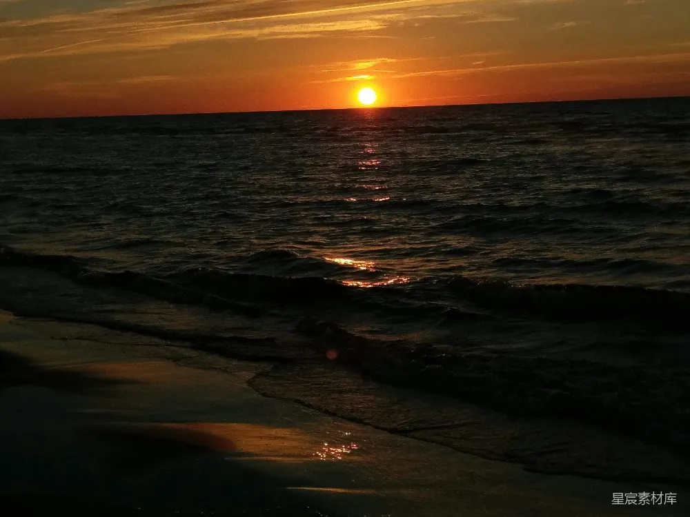高清摄影  夕阳正缓缓落下，映照在海滩上的水面上。
