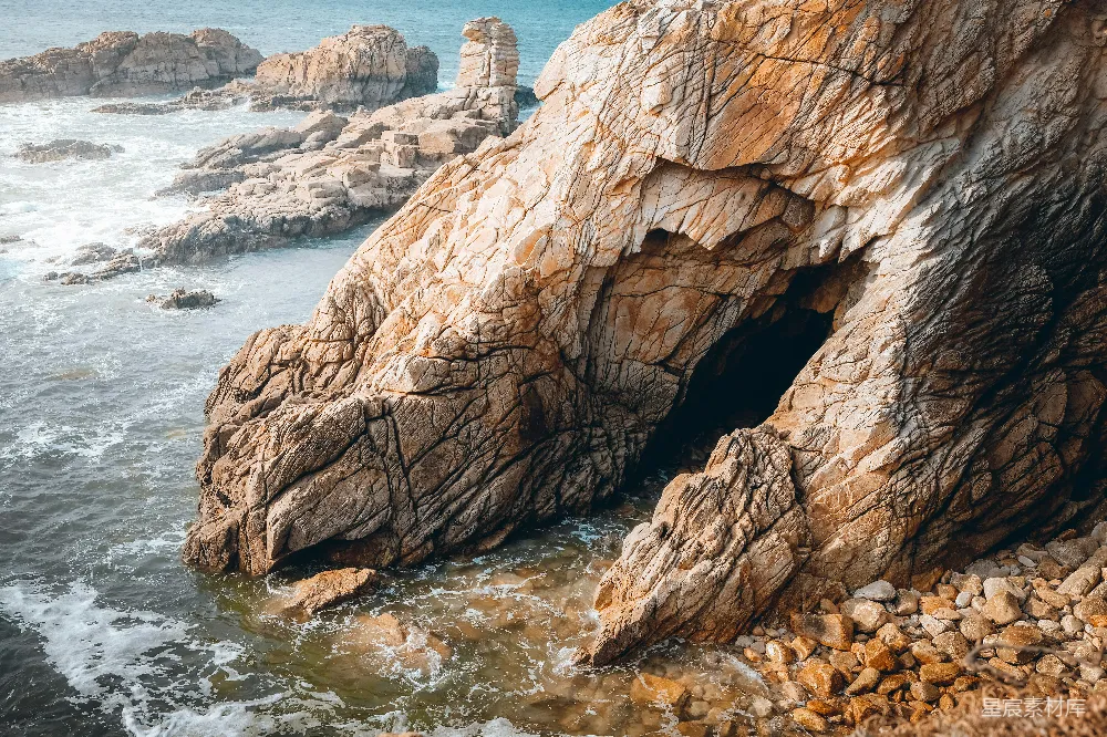 高清摄影 自然 一座巨大的岩石形成坐落在海滩上，旁边是海洋。