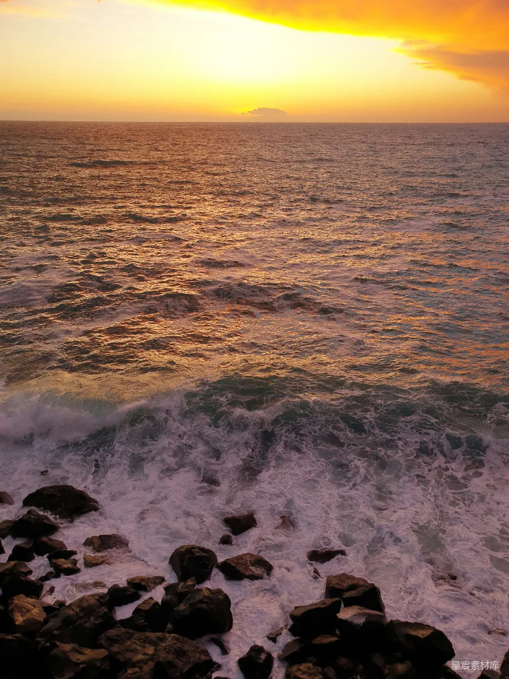 高清摄影  夕阳正缓缓落下，海面波光粼粼，前景中岩石隐约可见。