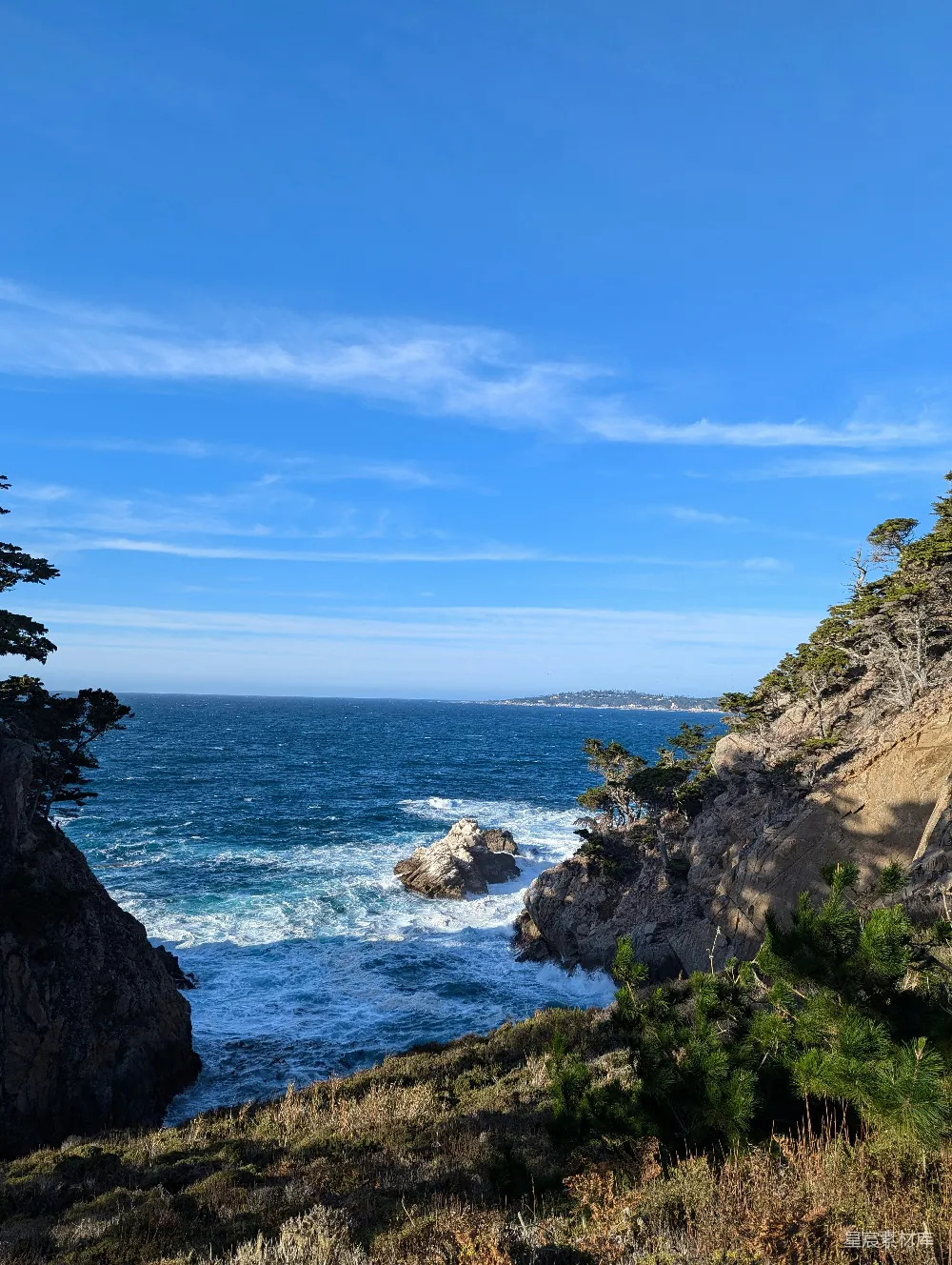 高清摄影  波浪在晴朗的蓝天背景下拍打着岩石海岸线。