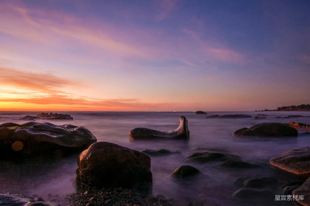 高清摄影  夕阳正在海洋上落下，前景中可以看到岩石。