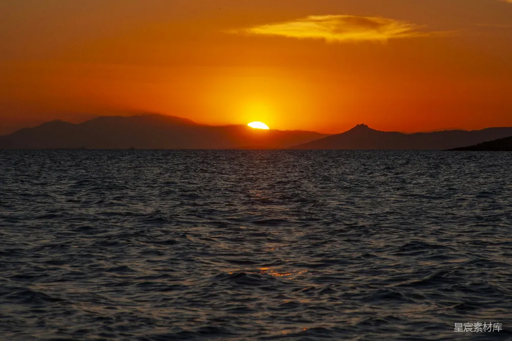 高清摄影  夕阳正挂在海洋上空，远处的山脉若隐若现。