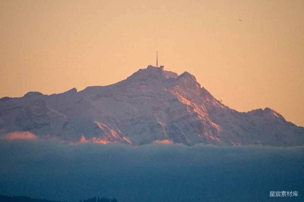 高清摄影  夕阳西下，雪山顶上矗立着一座无线电塔。