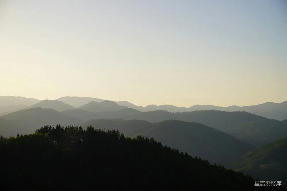高清摄影  一片山峦景色，前景中有树木。