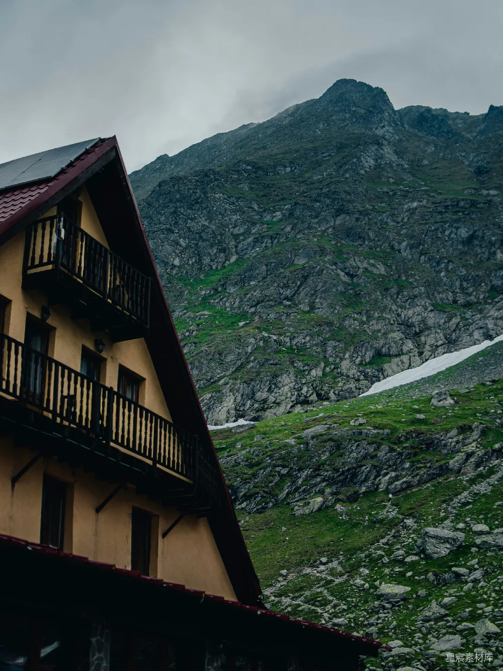 高清摄影  一座质朴的山间小屋矗立在布满雪迹的岩石山峰前。