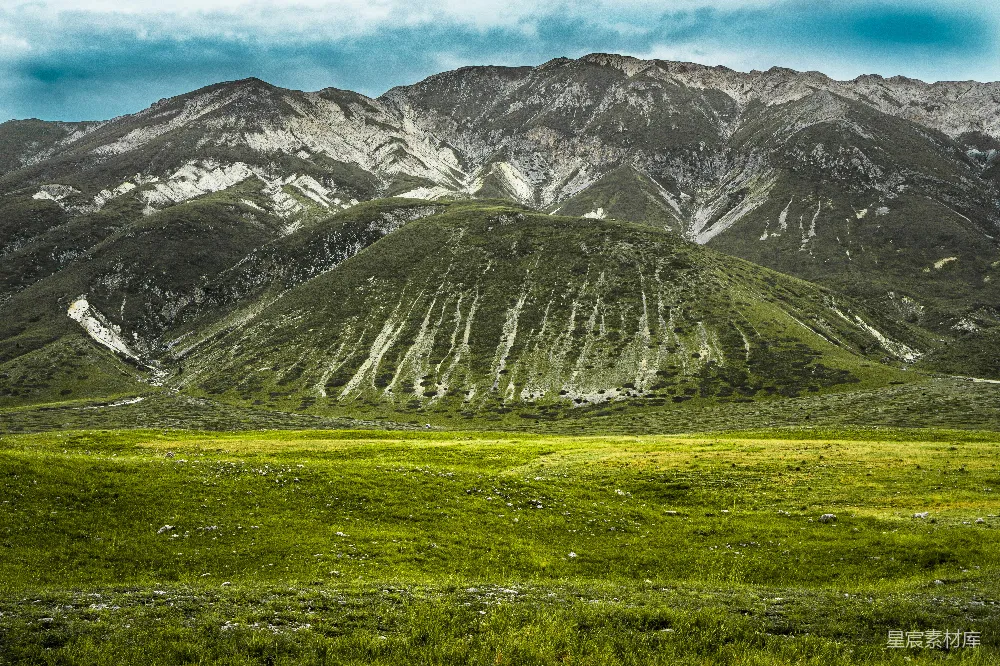 高清摄影  白天的雪山上有一片绿色的草地。