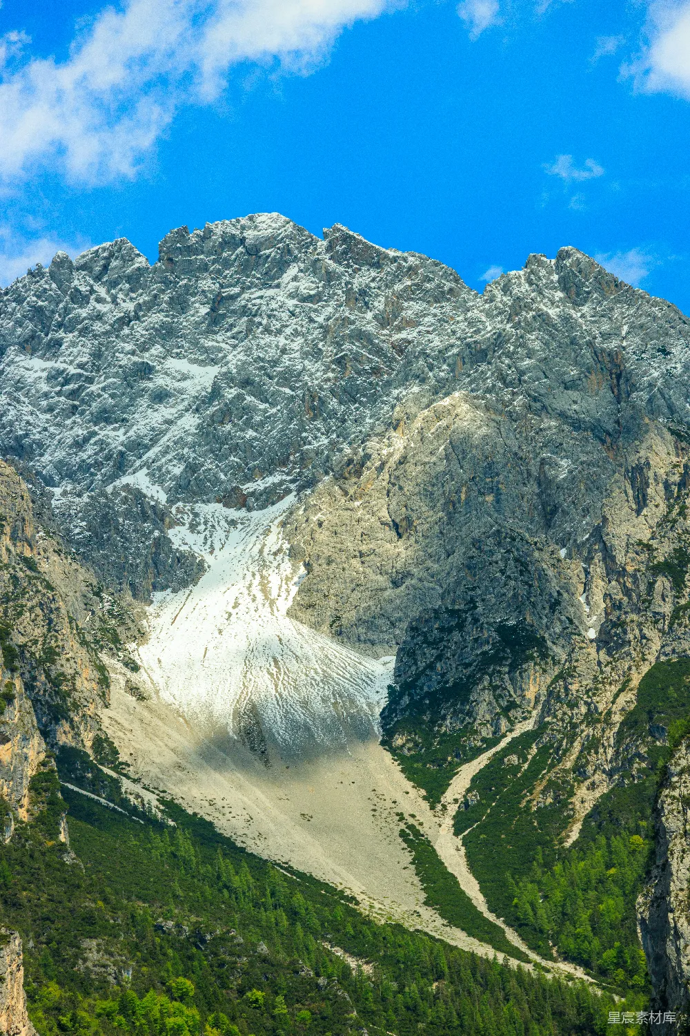 高清摄影  巍峨的雪山在蓝天白云下，山脚下是绿意盎然的山坡。