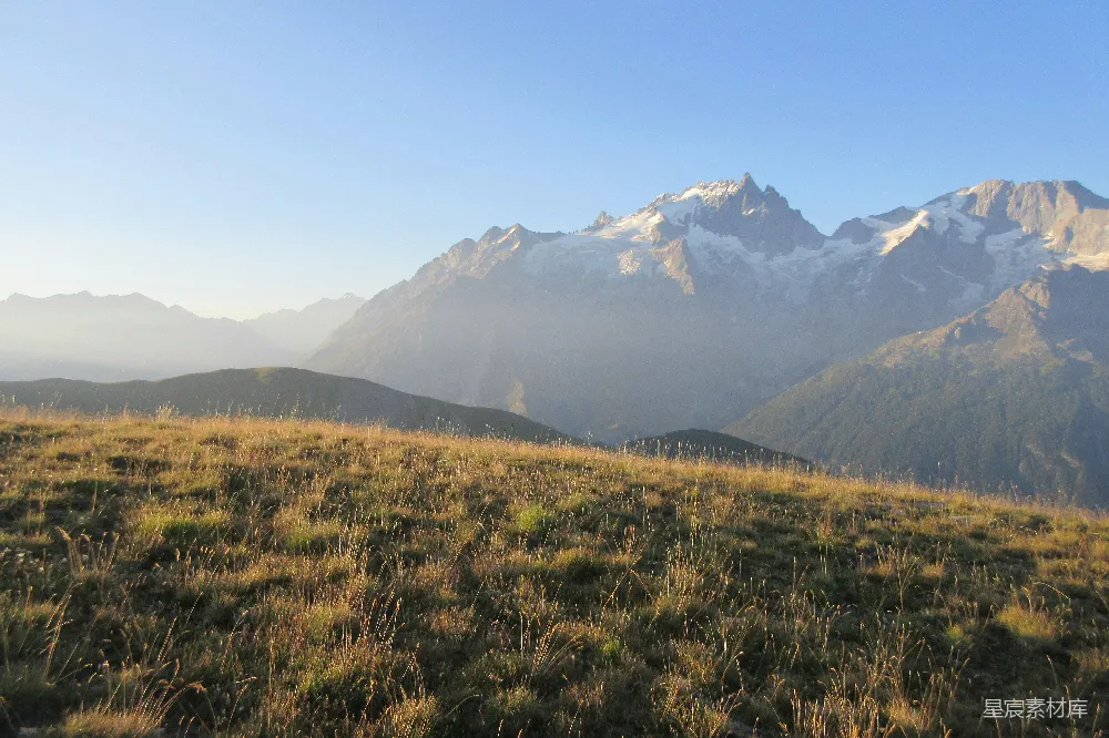 高清摄影  草地上前景，远处有雾气缭绕的山峦