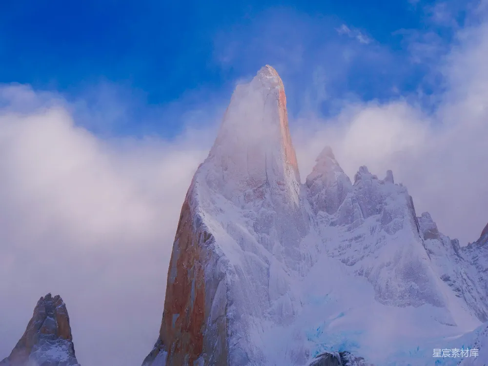 高清摄影  一座被白雪和云层覆盖的山峰在蓝天之下