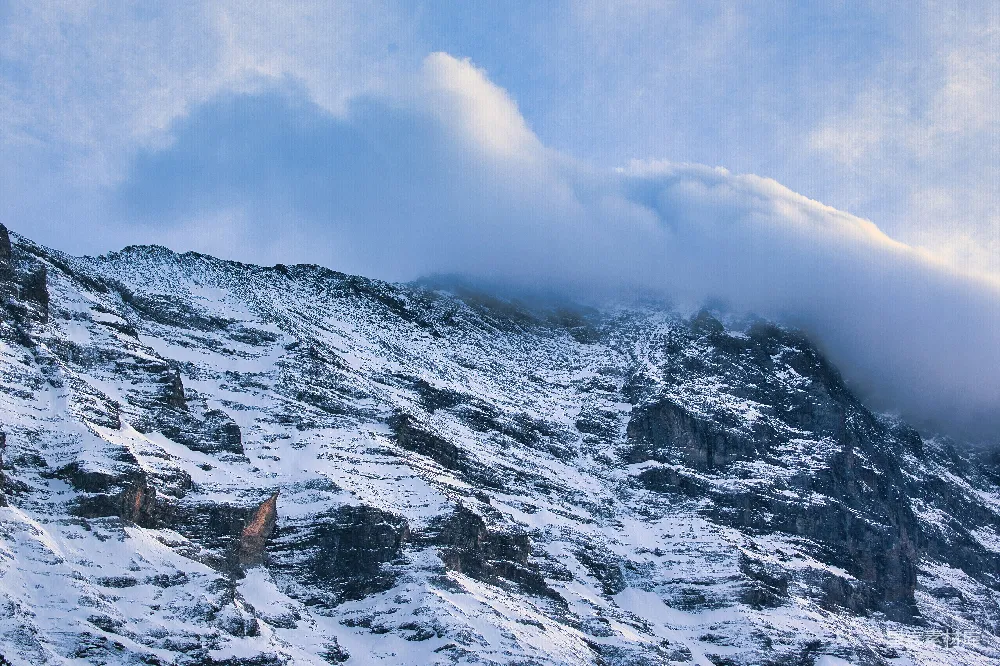 高清摄影  一座被积雪和云雾覆盖的山峰，在蓝天的映衬下。