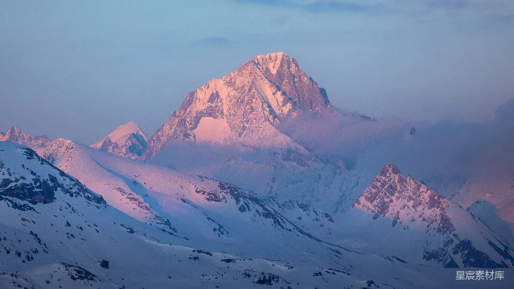高清摄影  雪山峰顶被柔和的粉红色日出光线照亮。
