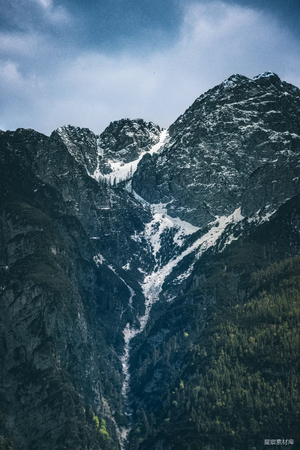 高清摄影  白雪皑皑的山峰在多云的天空下衬着绿树。