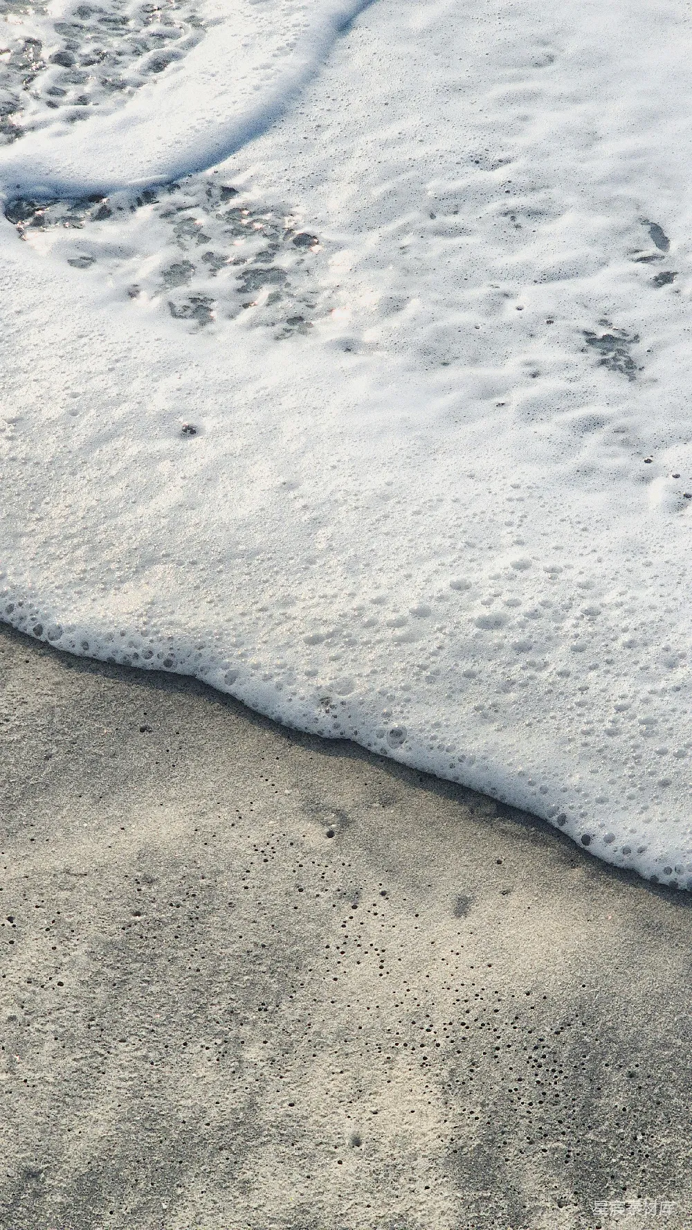 高清摄影  白色的海浪泡沫拍打在沙滩上。