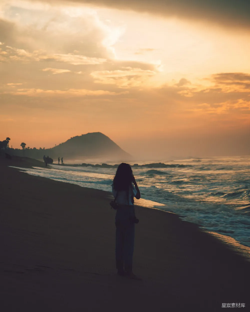 高清摄影  一个穿着黑色夹克的女人站在海边，夕阳西下。