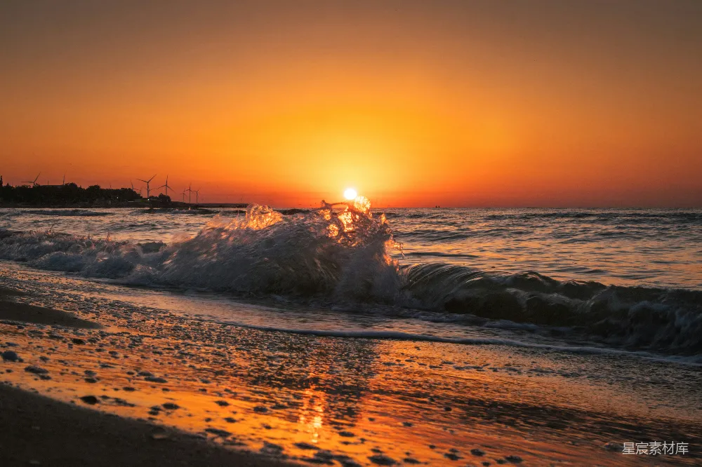 高清摄影  夕阳正缓缓落下，洒落在海滩上的水面上。