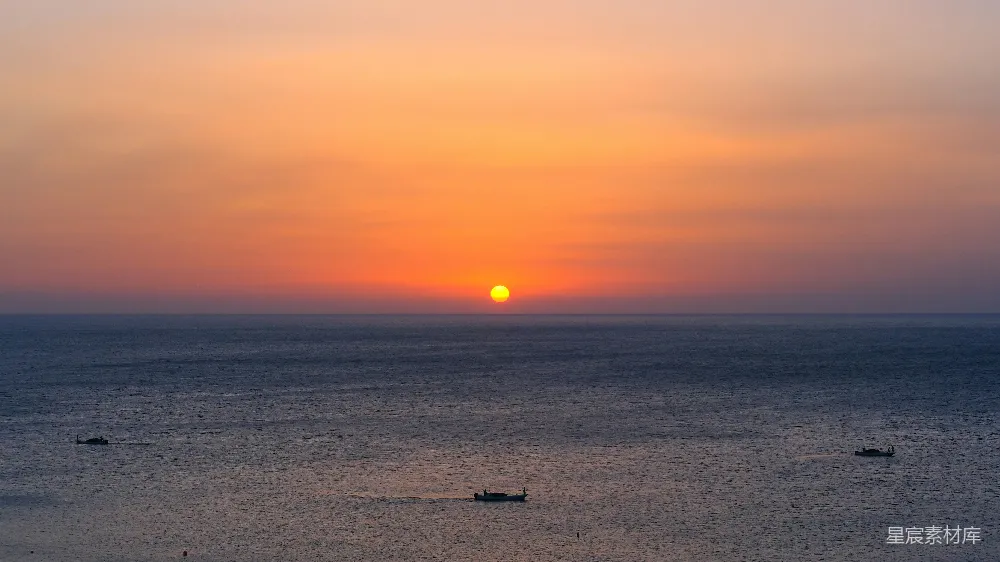 高清摄影  平静的海面上的日落景色，远处有几艘船