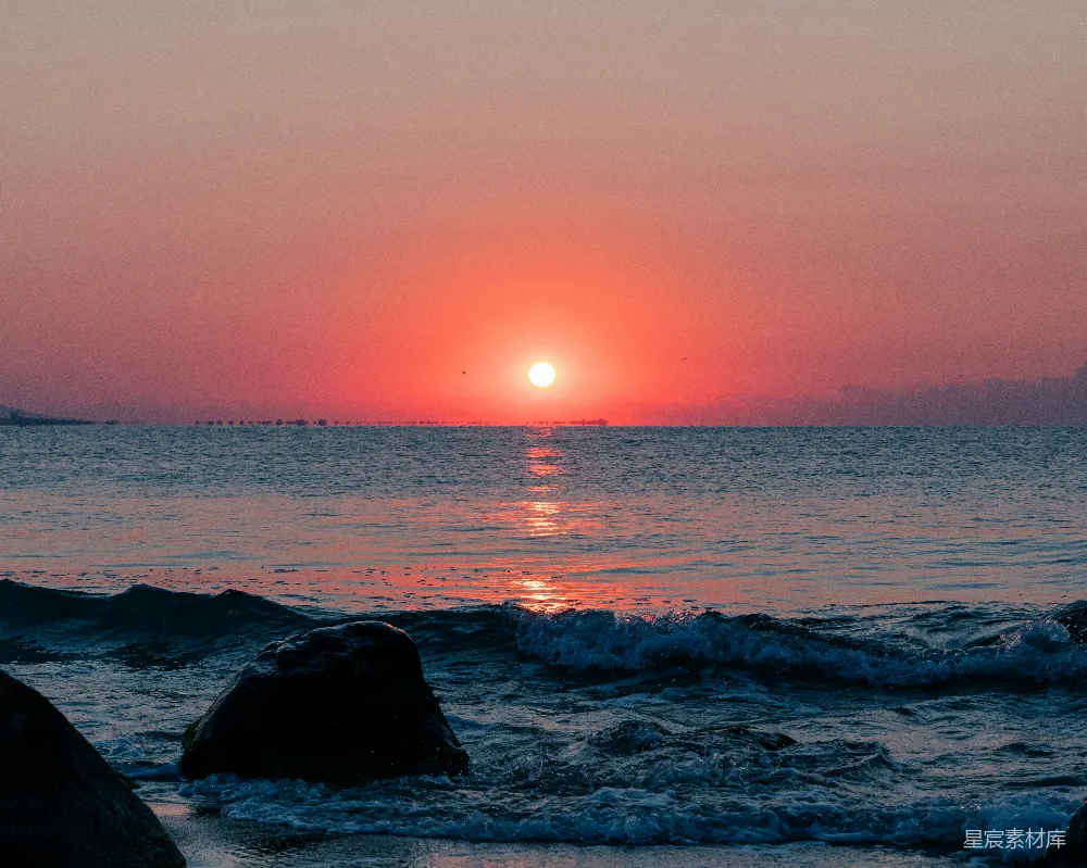 高清摄影  夕阳正从海平面上落下，前景中可以看到岩石。
