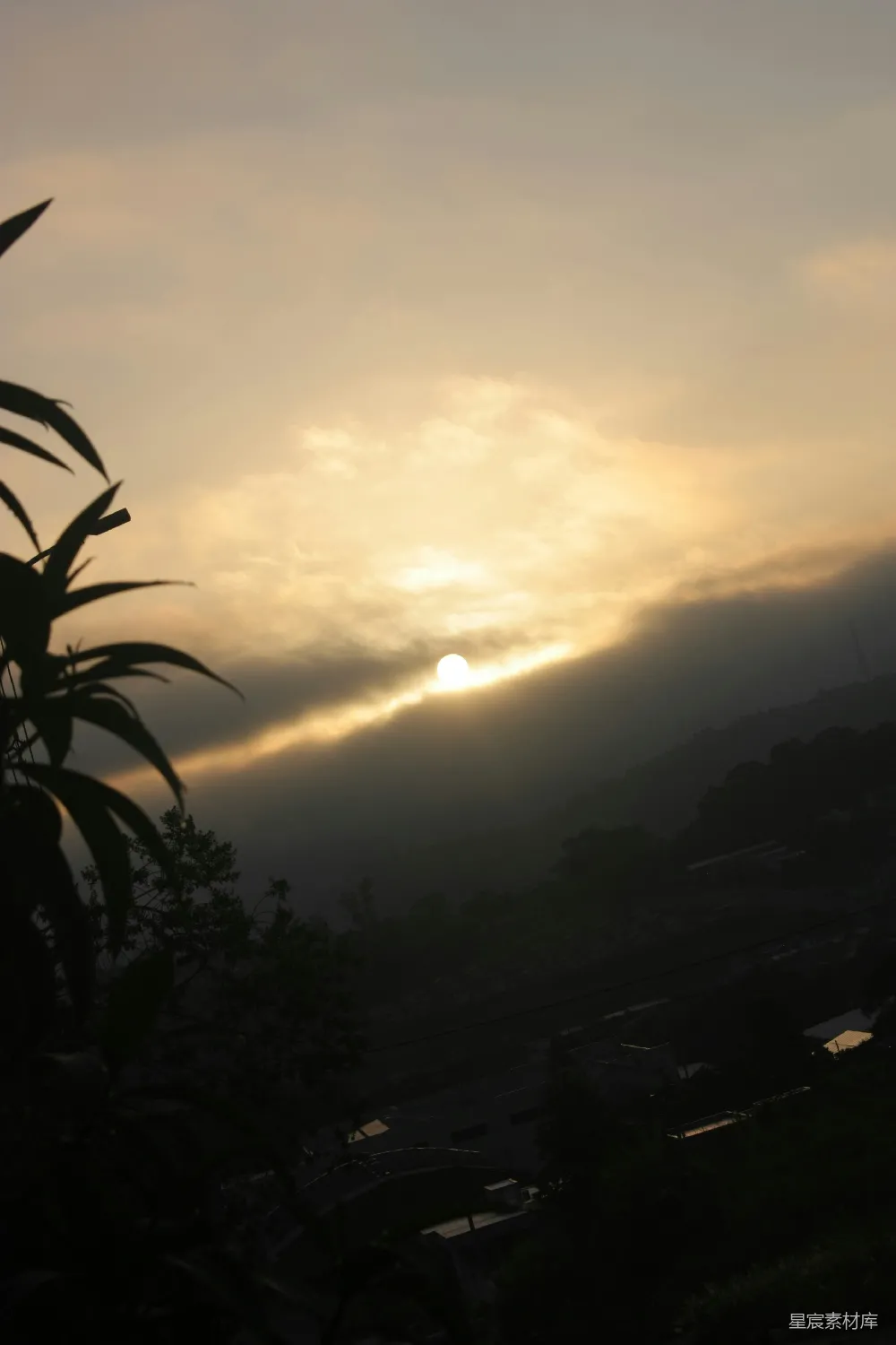高清摄影  夕阳落在薄雾缭绕的群山之后，树木剪影清晰。