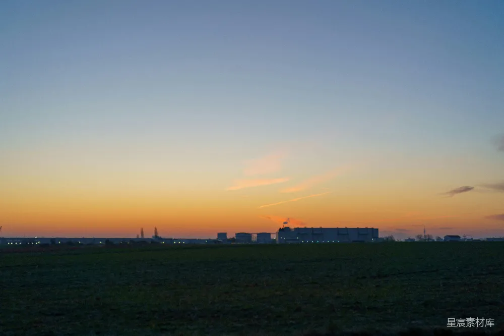 高清摄影  夕阳正在一片田野上落下，背景中有建筑物。